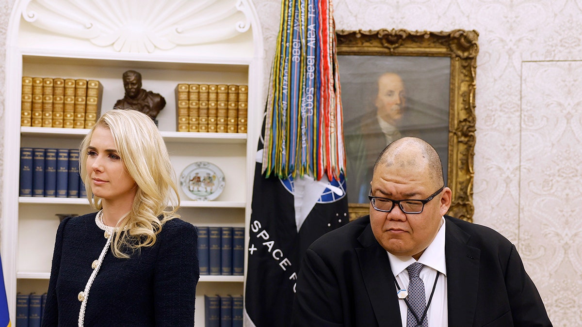 Trump aides Natalie Harp and Stephen Cheung listen as President Trump signs executive orders in the White House.