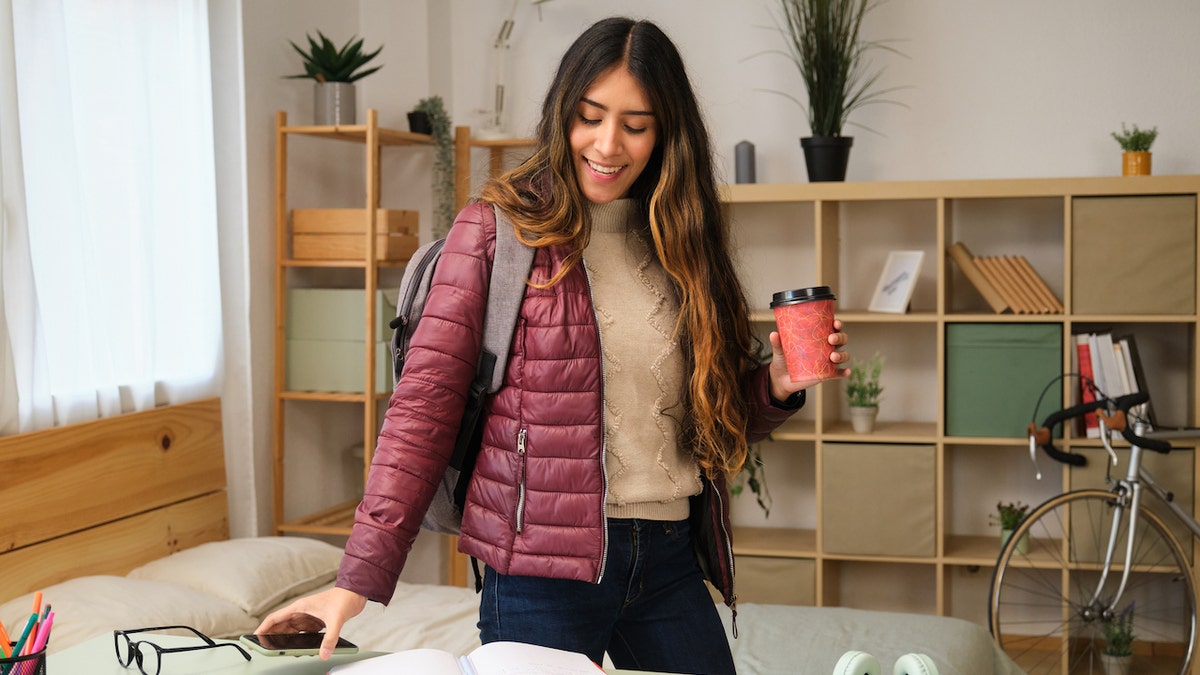 Smiling university student getting ready to leave for class with a backpack and coffee