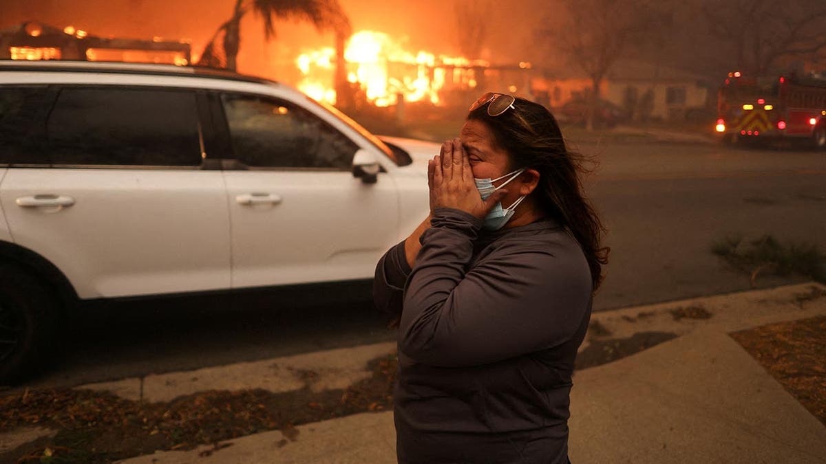 woman crying on sidewalk, fire raging behind her