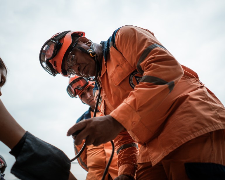 Edgar Larga — member of the Defensa Civil Colombiana, dressed in an orange uniform and helmet — takes the blood pressure of a recently arrived woman from Catatumbo.