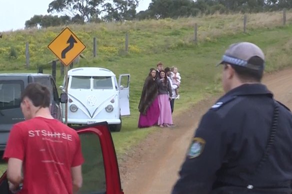 Wedding guests stand on the side of the road after a vehicle transporting attendees went off the road.