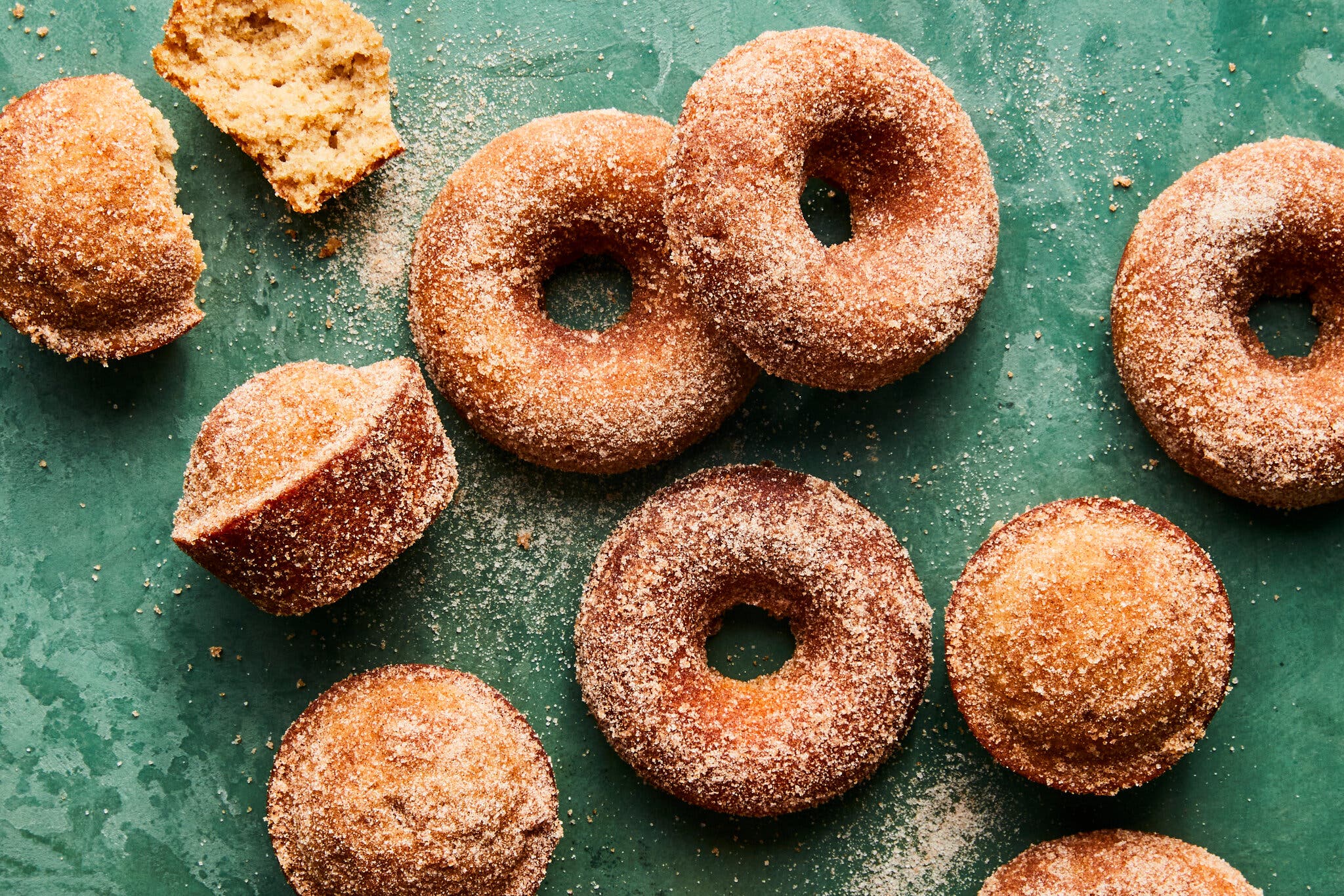 An overhead image of doughnuts and muffins tossed with cinnamon sugar against a green background.