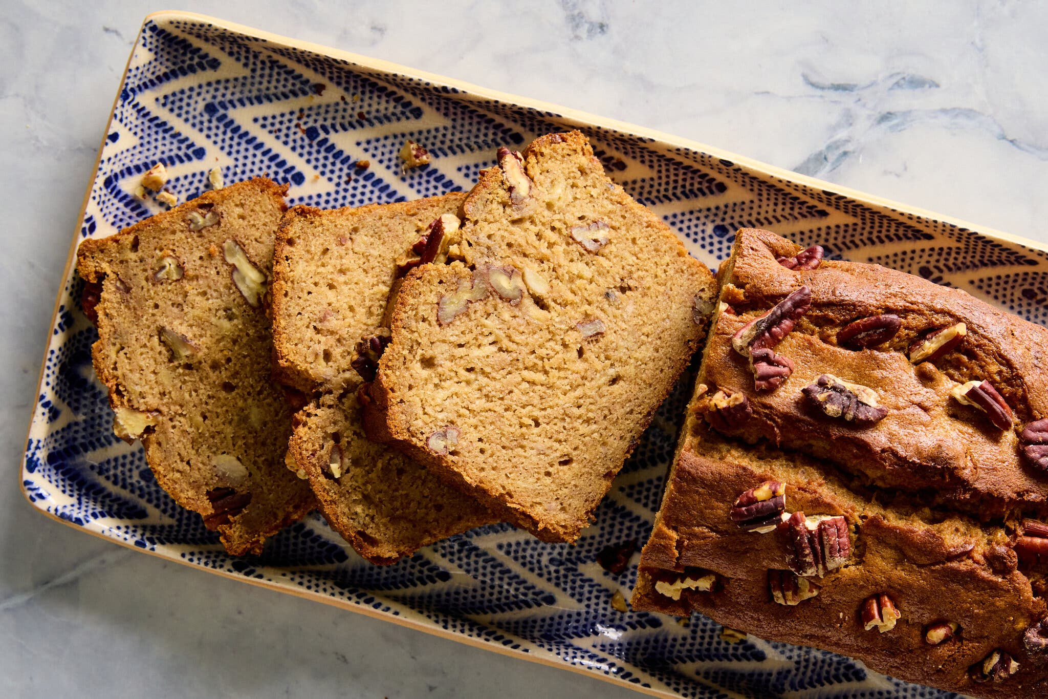 An overhead image of a pecan studded loaf on a blue and white platter.