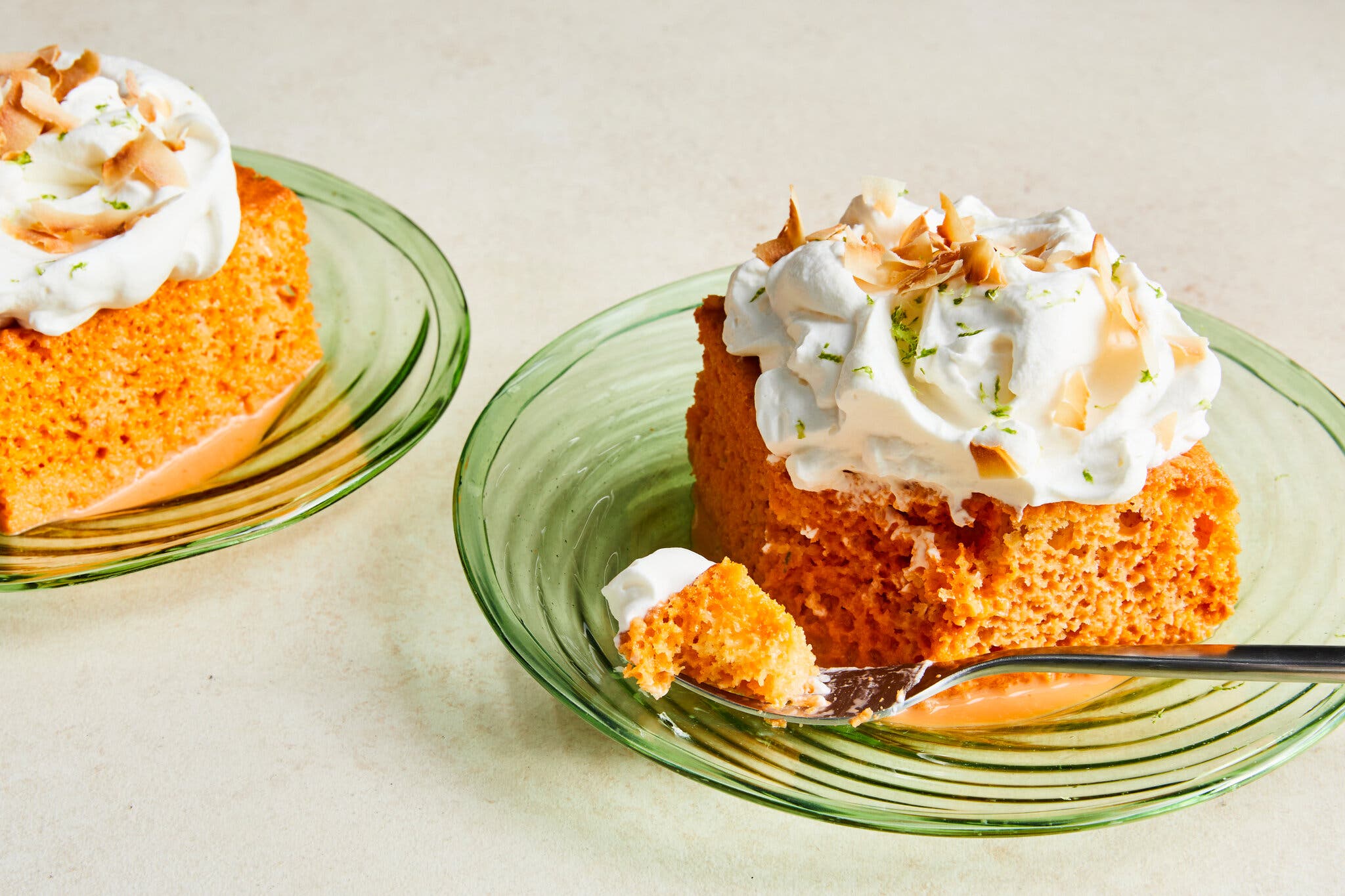 A side image of an orange, cream-topped tres leches cake finished with lime zest and coconut.