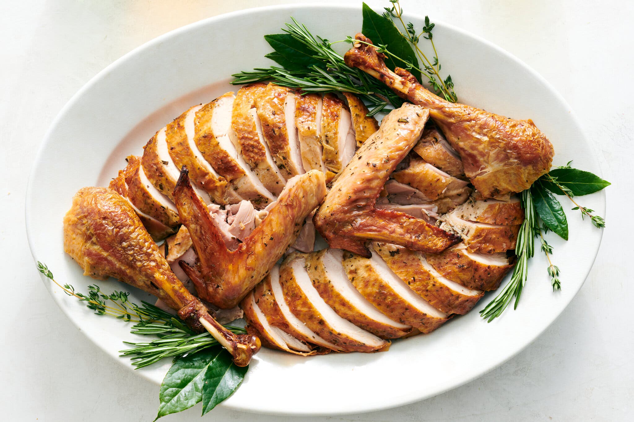 An overhead image of a carved turkey on a platter and surrounded by herbs.