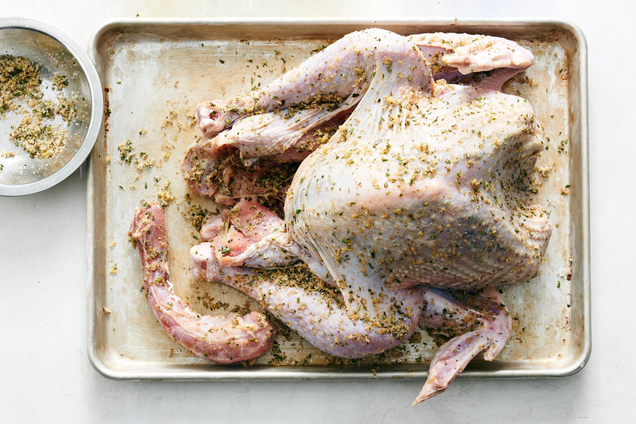 An overhead image of a raw turkey coated in brine on a sheet pan.