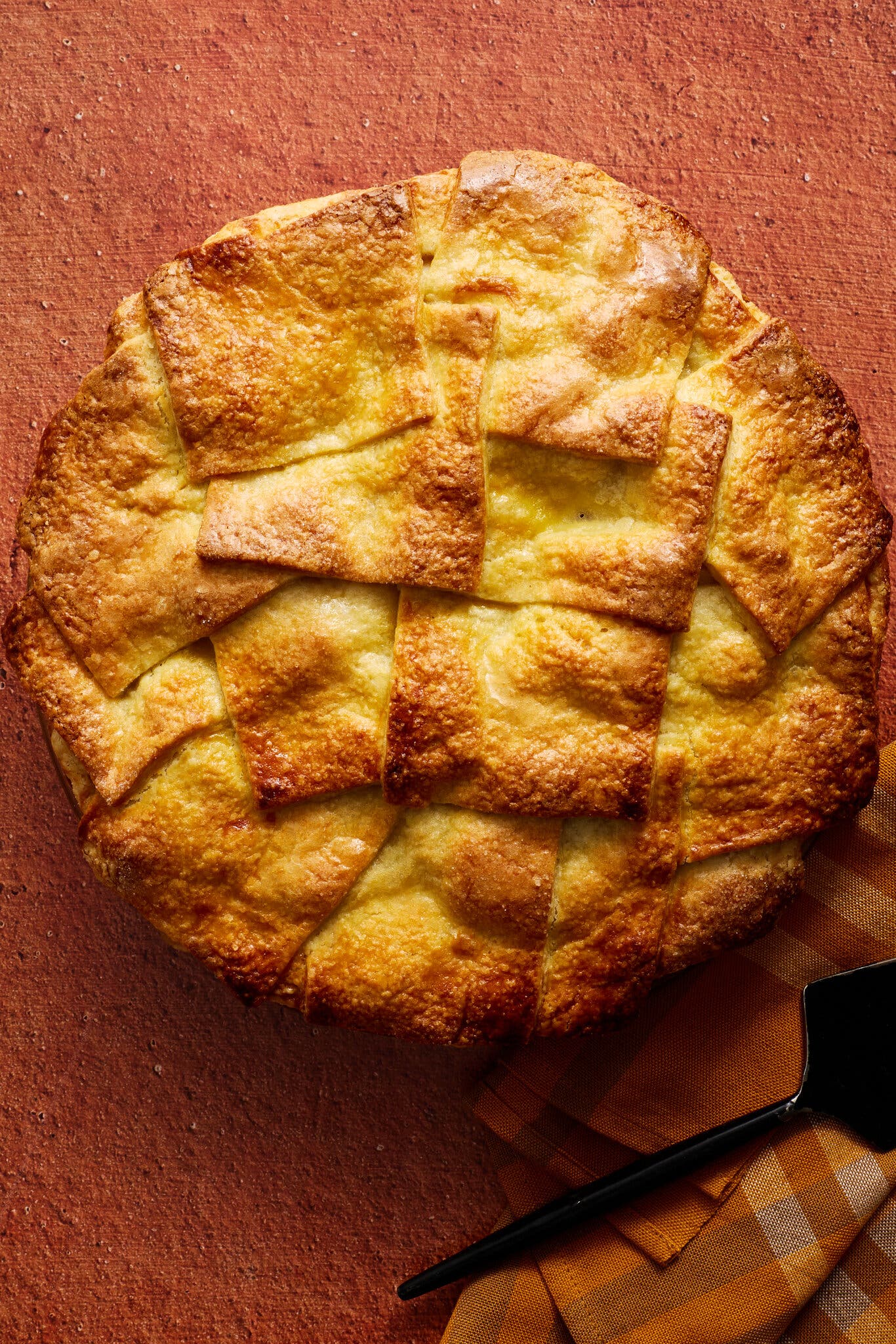 An overhead shot of a pie with a golden shingled crust that sits against a dark orange background.