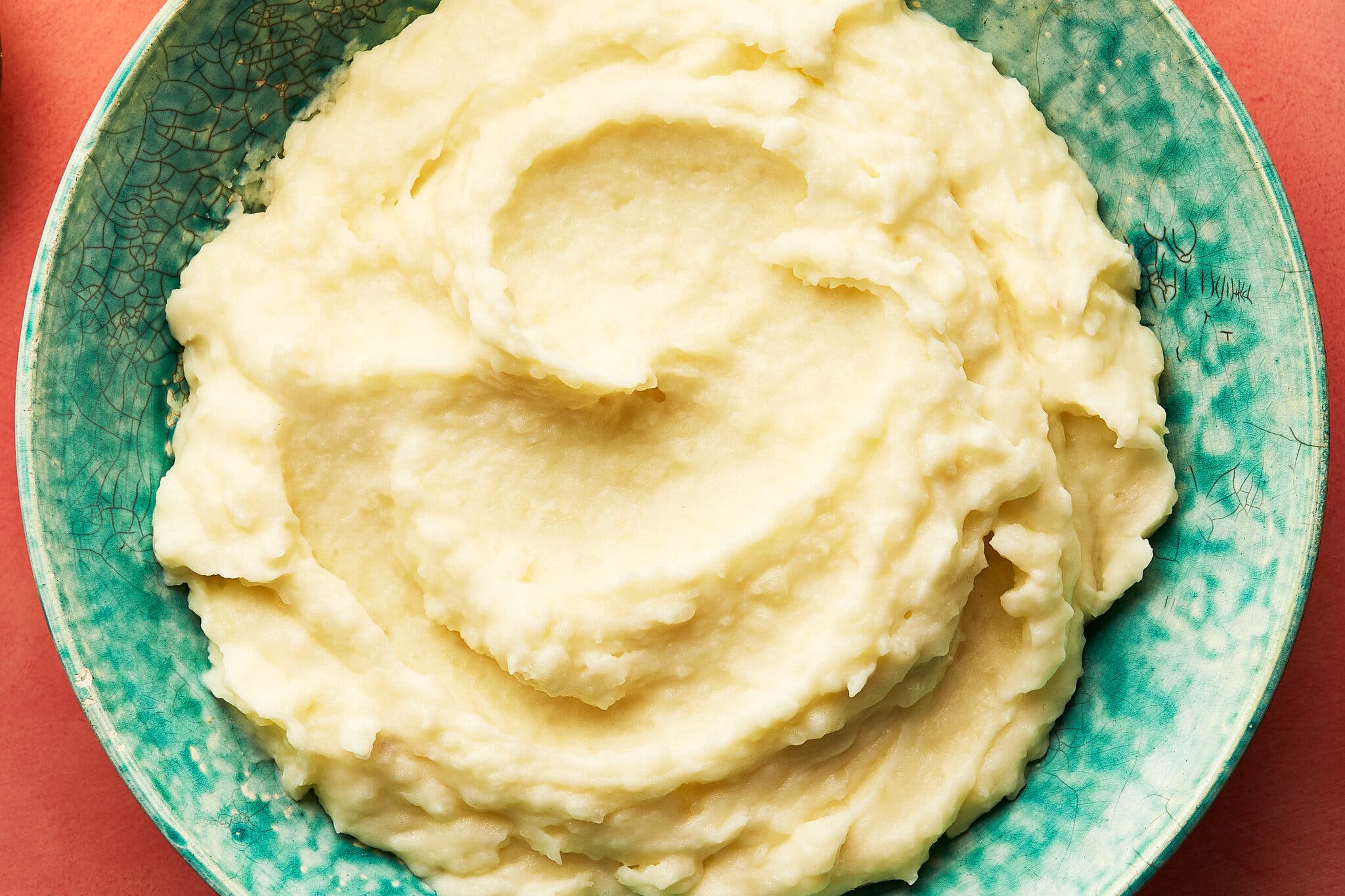 An overhead image of a light green serving bowl filled with mashed potatoes. 