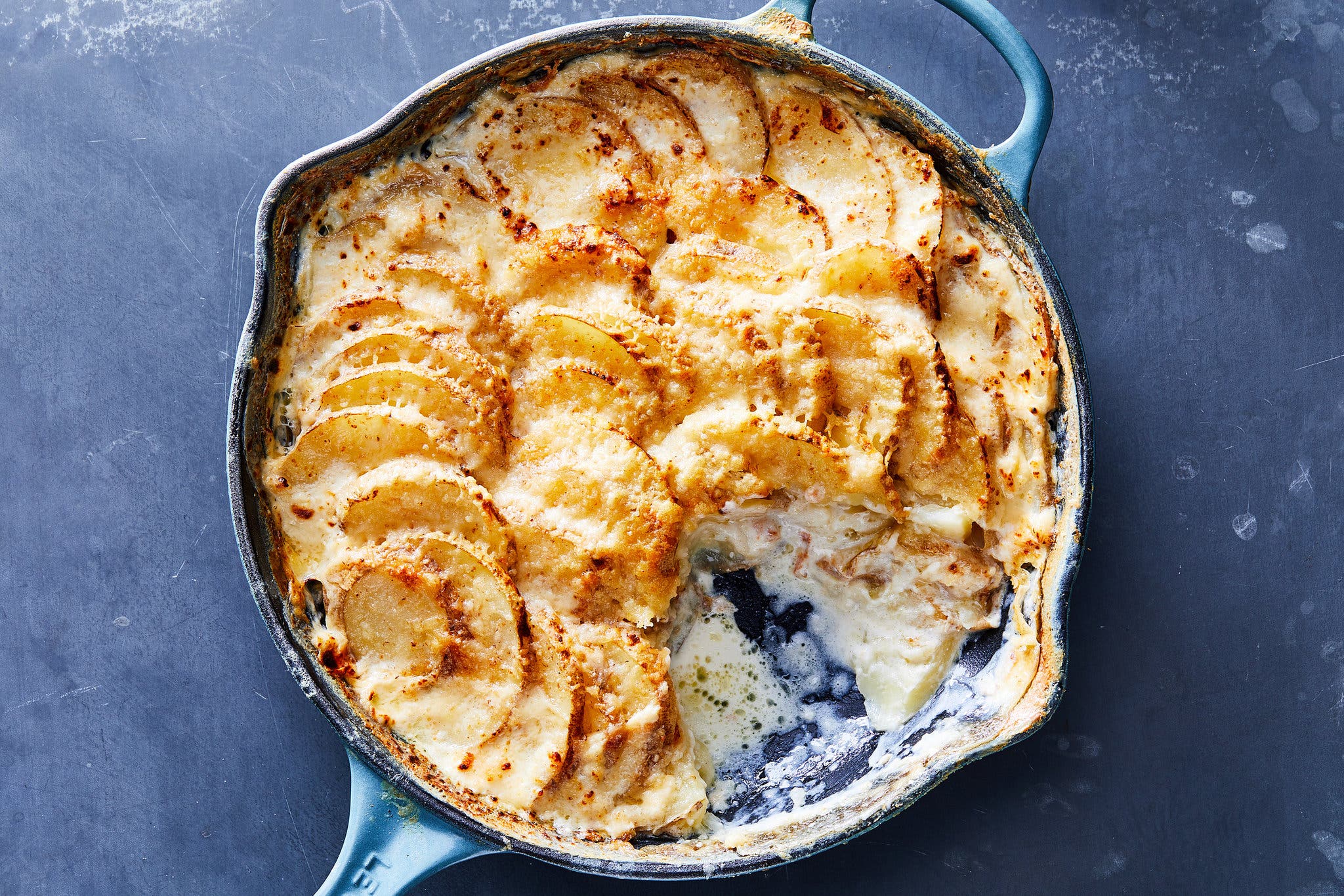 An overhead image of a light blue enamel skillet on a dark gray background filled with creamy scalloped potatoes. 