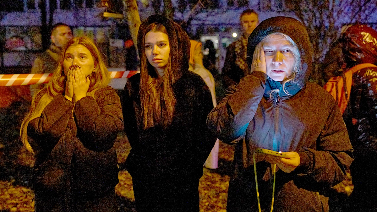 People stand outside, watching a building engulfed in flames after a nighttime drone strike.