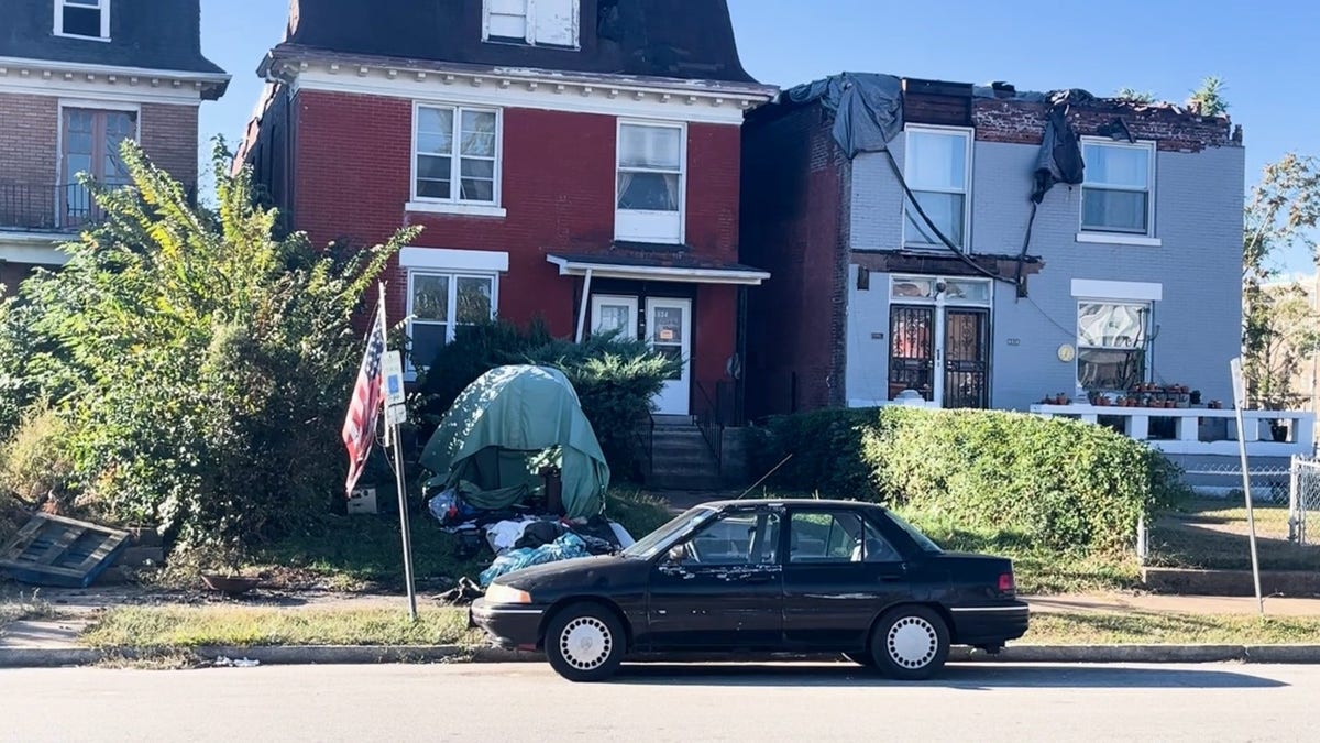 A damaged St. Louis home with a tent in the front yard where someone appears to be camping on the property months after the tornado.