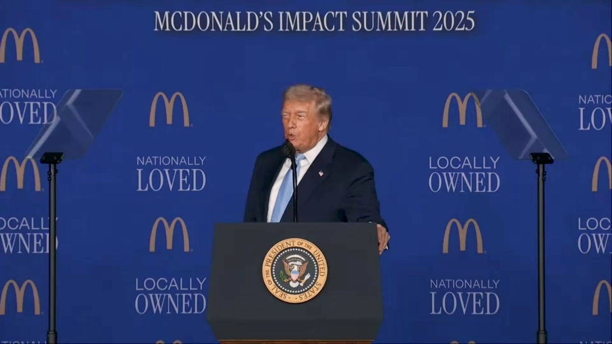 President Donald Trump speaks in front of a podium behind a backdrop showing the McDonald's logo.