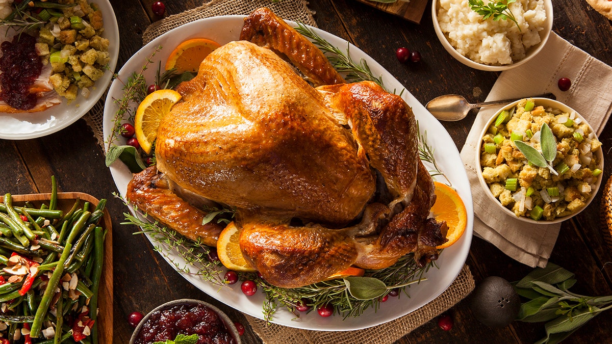 A roasted Thanksgiving turkey surrounded by side dishes including stuffing, mashed potatoes, green beans and cranberry sauce.