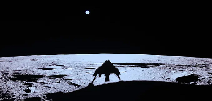 The shadow of a moon lander is seen on the surface of the moon while a round circle, Earth, hangs in the dark beyond the moon.