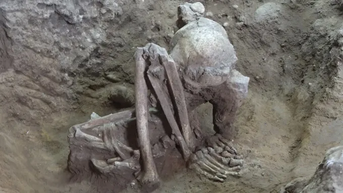 A hunched over mummified skeleton on a patch of dirt