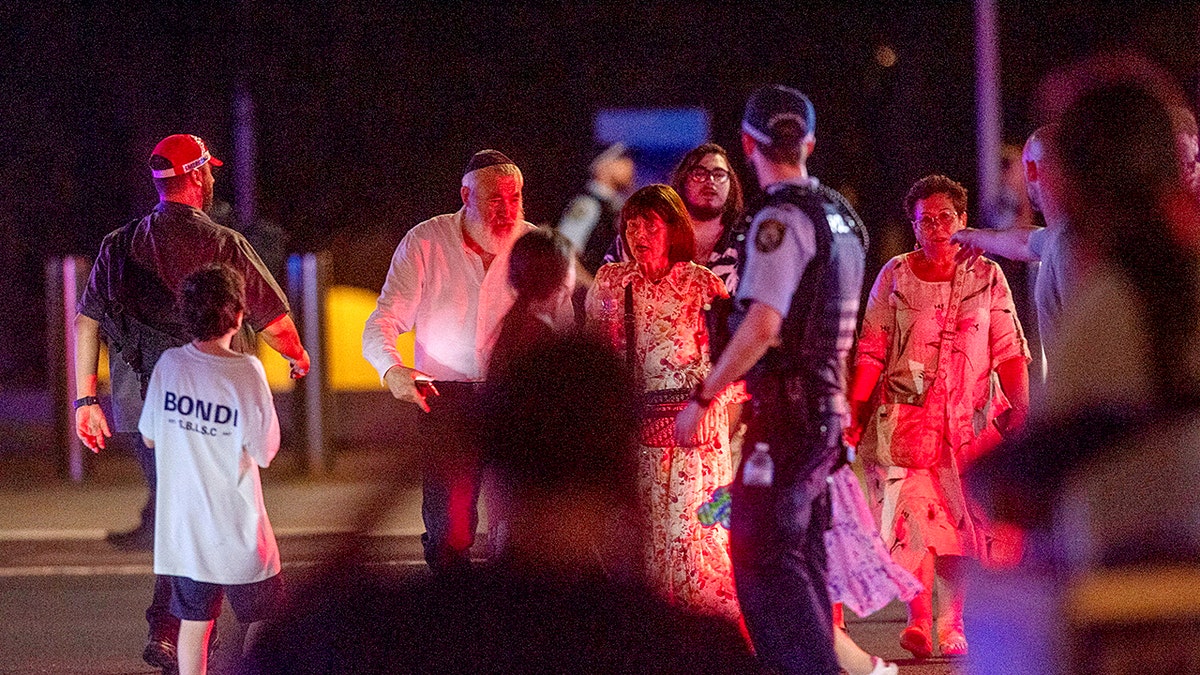 People walk as police officers stand guard on the street following a shooting incident at Bondi Beach, in Sydney, Australia, Dec. 14, 2025.