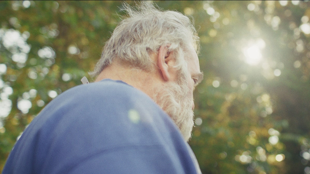 Over the shoulder shot of Mike Carroll outside in his yard with the sun shining through trees behind him.