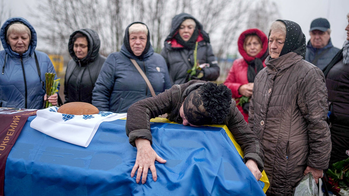 A grieving parent mourns beside a soldier’s coffin during a funeral service.