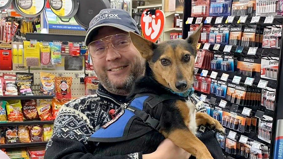 Anthony James Kazmierczak holds a dog and smiles whilst in a store.