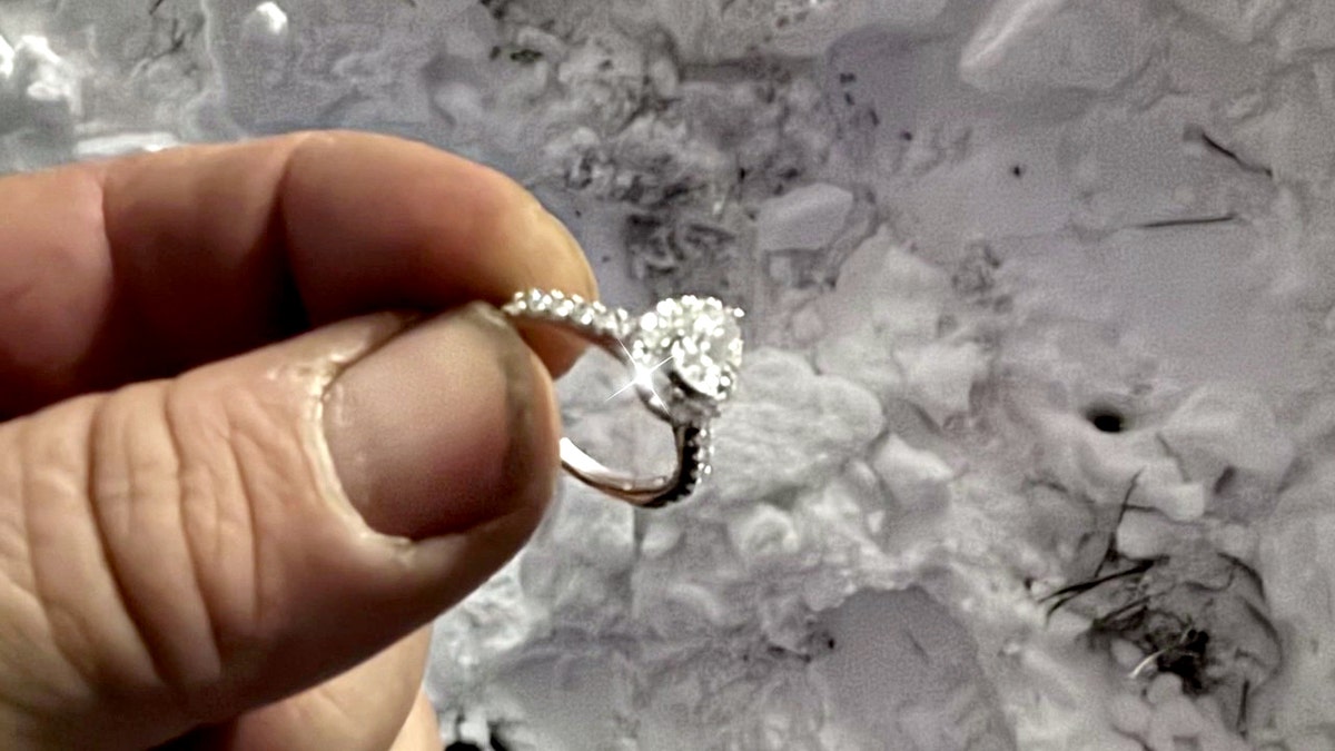 fingers holding engagement ring above the snowy ground