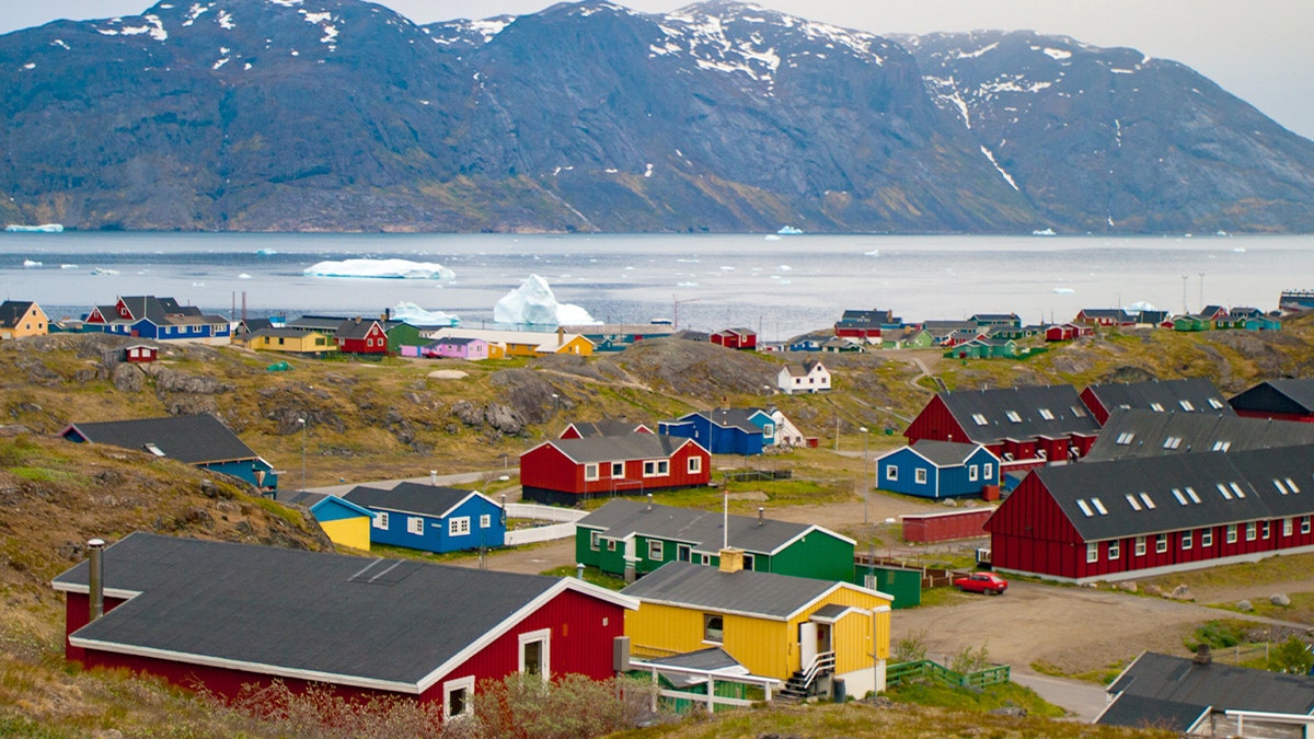 Colorful houses line the shoreline of a small Greenlandic village surrounded by rugged landscape.