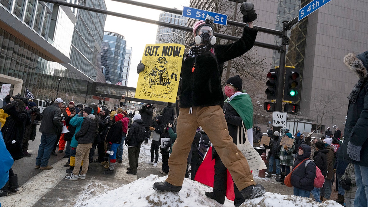 An anti-ICE agitator in Minneapolis holds a sign reading "OUT. NOW."