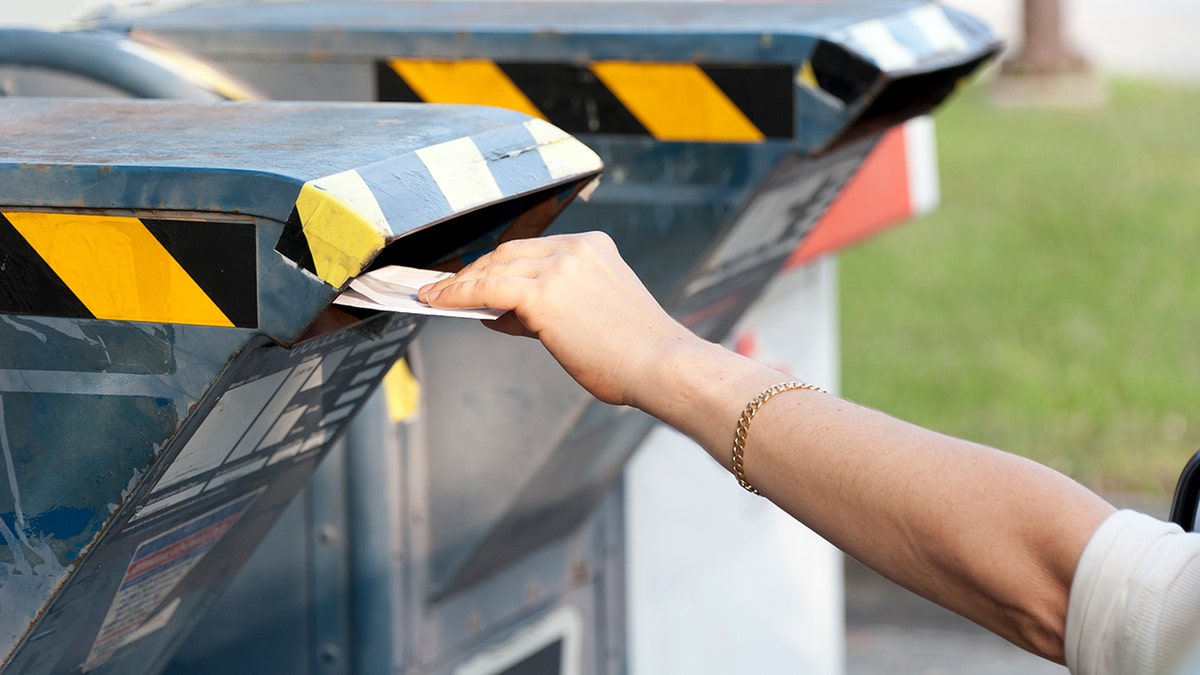 Person placing mail into a residential mailbox slot on a metal community mailbox.