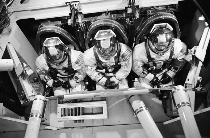 Three astronauts in space suits sitting in a machine