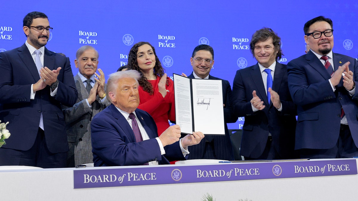 The U.S. president raises a signed document during a formal diplomatic event at an international forum.