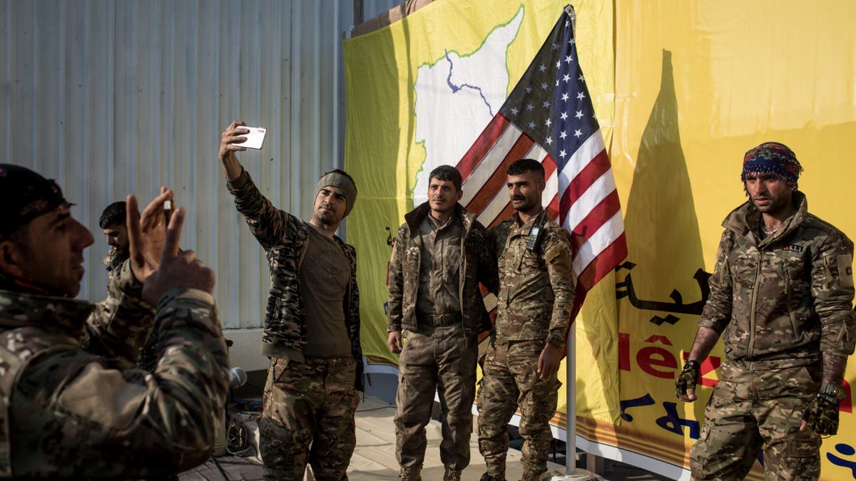 Syrian Democratic Forces (SDF) fighters pose for a photo with the American flag on stage after a SDF victory ceremony announcing the defeat of ISIL in Baghouz was held at Omer Oil Field on March 23, 2019 in Baghouz, Syria.