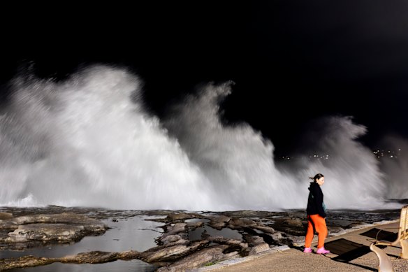 A person walks past large breaking waves at Clovelly Beach before sunrise on Saturday morning.