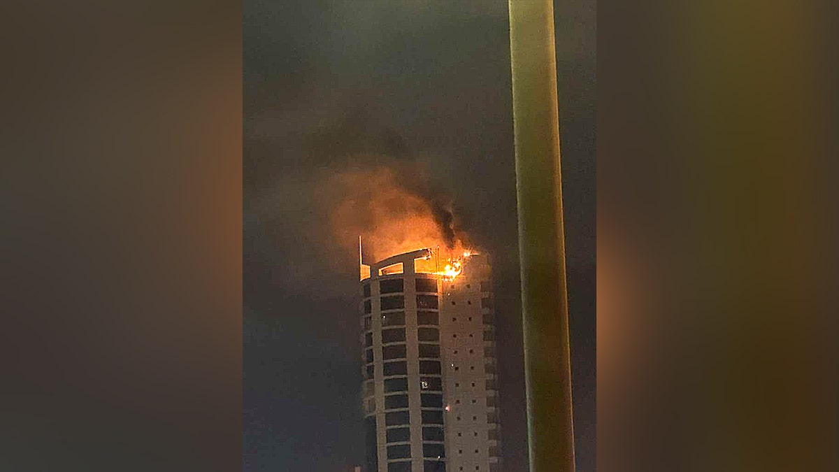 flames and smoke billow from the top of a high-rise building