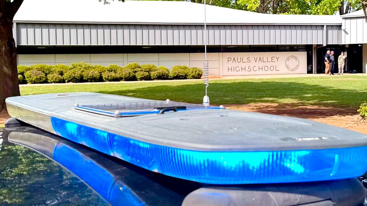 roof of a police car in the foreground as law enforcement stands outside Pauls Valley High School