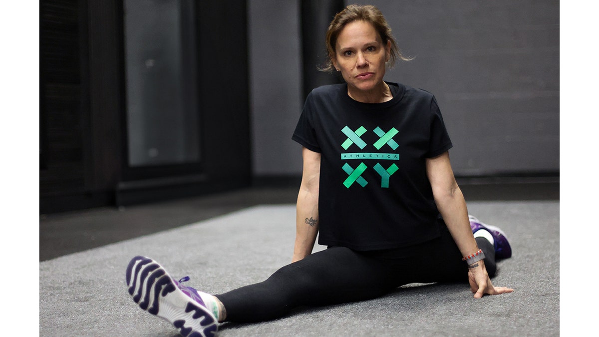 Jennifer Sey standing on a gym floor performing a split