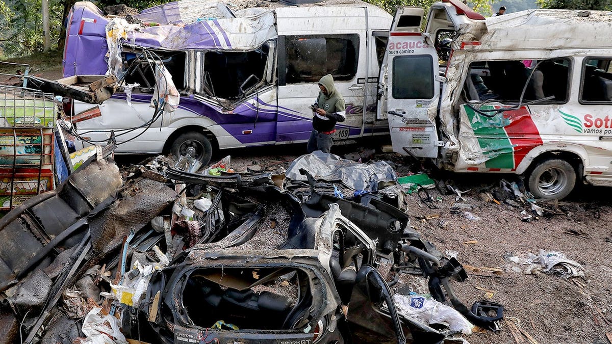 A man stands in the middle of wreckage from a bus explosion.