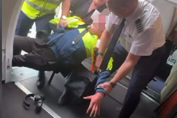 A still from footage of the boy being restrained by a Jetstar worker, passenger and the pilot.