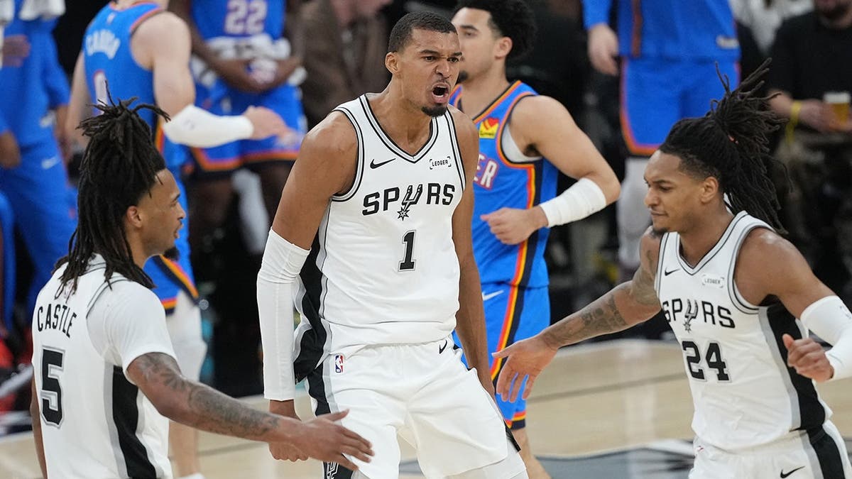 Stephon Castle, Victor Wembanyama, and Devin Vassell reacting during an NBA game in San Antonio