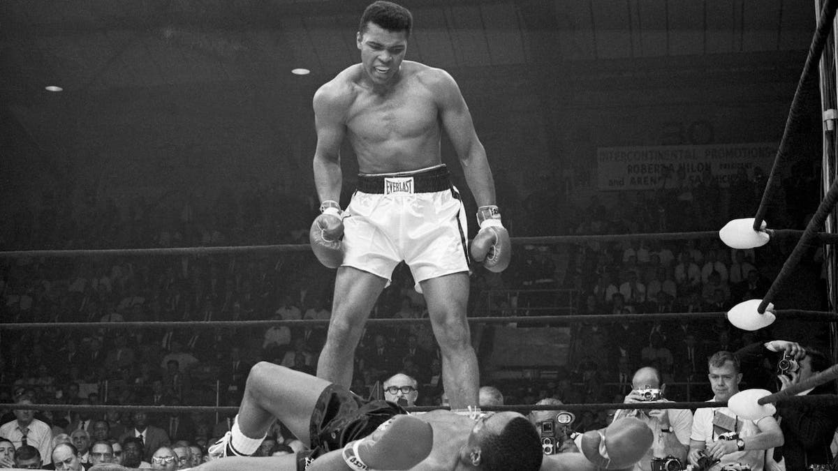 Heavyweight champion Muhammad Ali standing over Sonny Liston in a boxing ring.