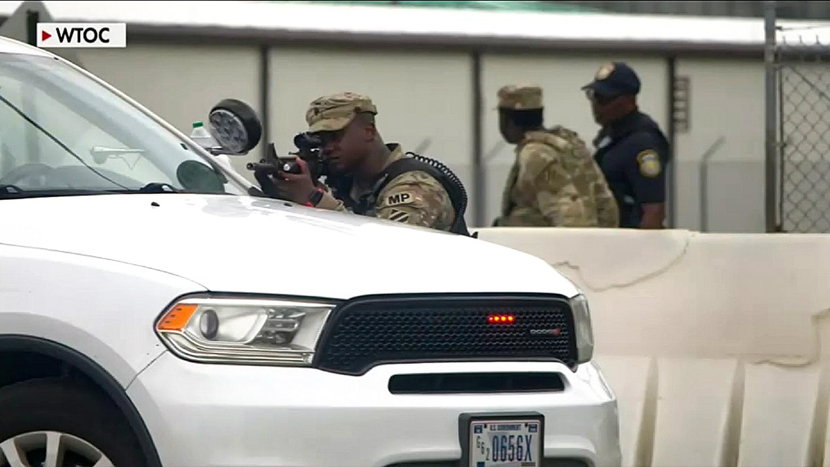 A soldier armed and standing behind a white vehicle at Fort Stewart, Georgia.