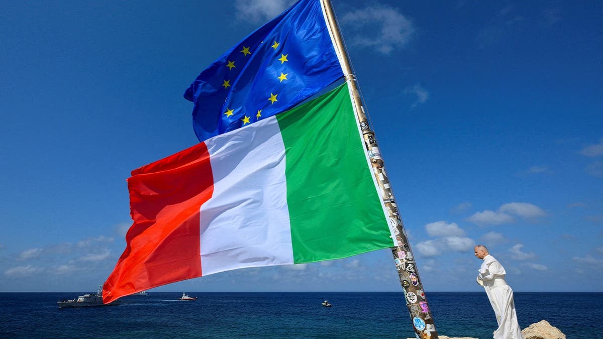 Pope Leo stands next to the European Union and Italy's flags as he visits the island of Lampedusa, a key entry point for migrants crossing the Mediterranean Sea, during a pastoral trip, Italy, July 4, 2026.