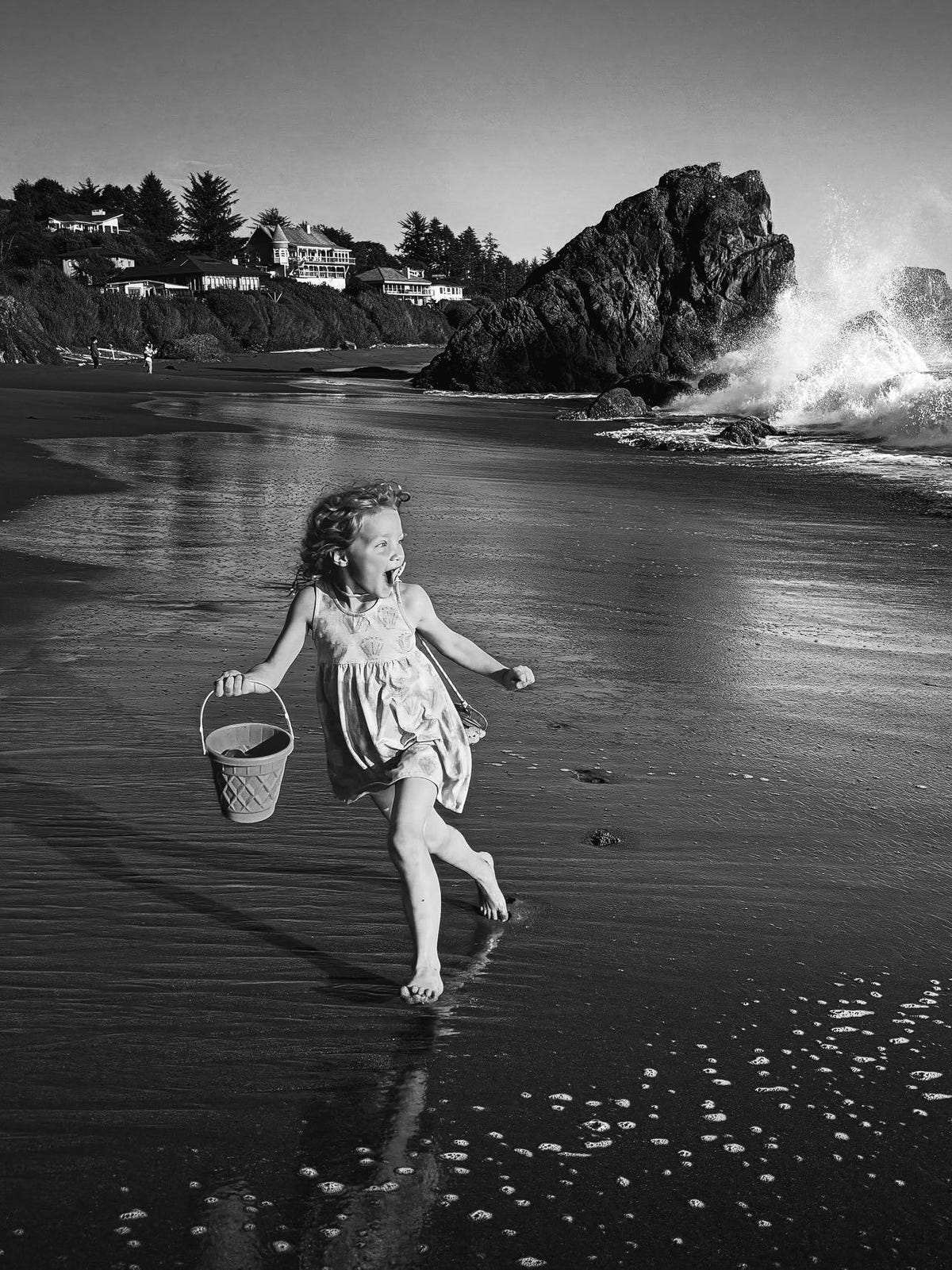 A young girl runs on a beach carrying a bucket.