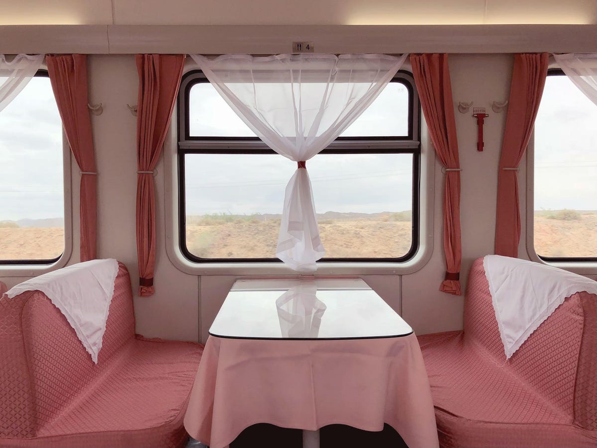 A table in a train car where the upholstry and curtains are pink.