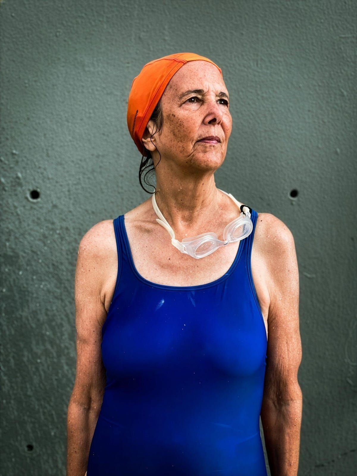 A woman in a blue swimsuit, orange swim cap and goggles looks to the side.