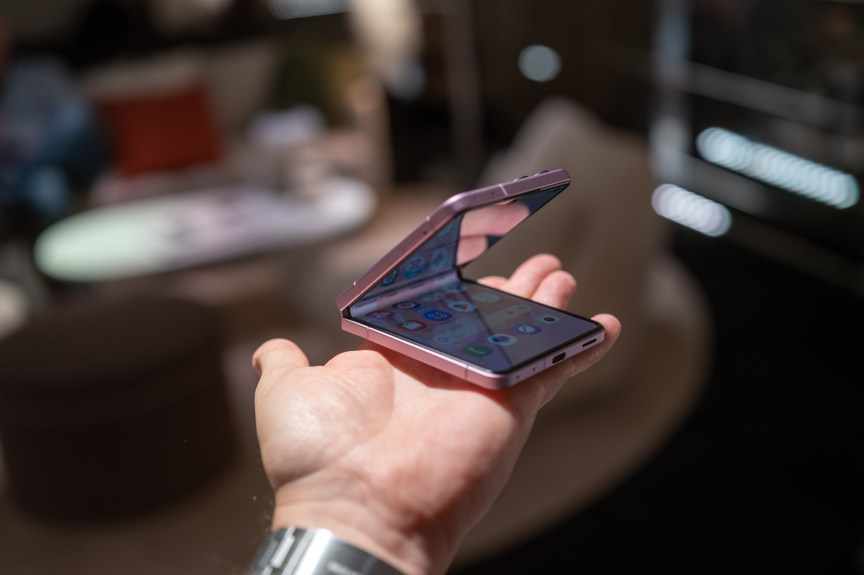 A small flip-style phone held in a person's hand.