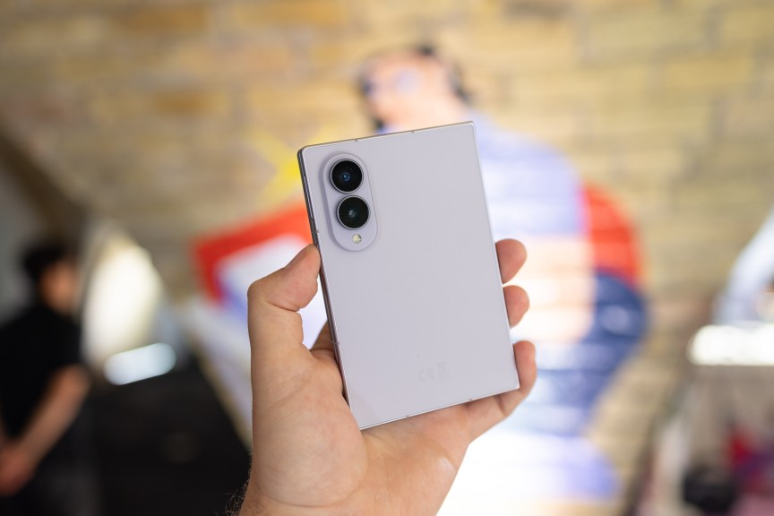 A compact folding phone is held closed in a person's hand.