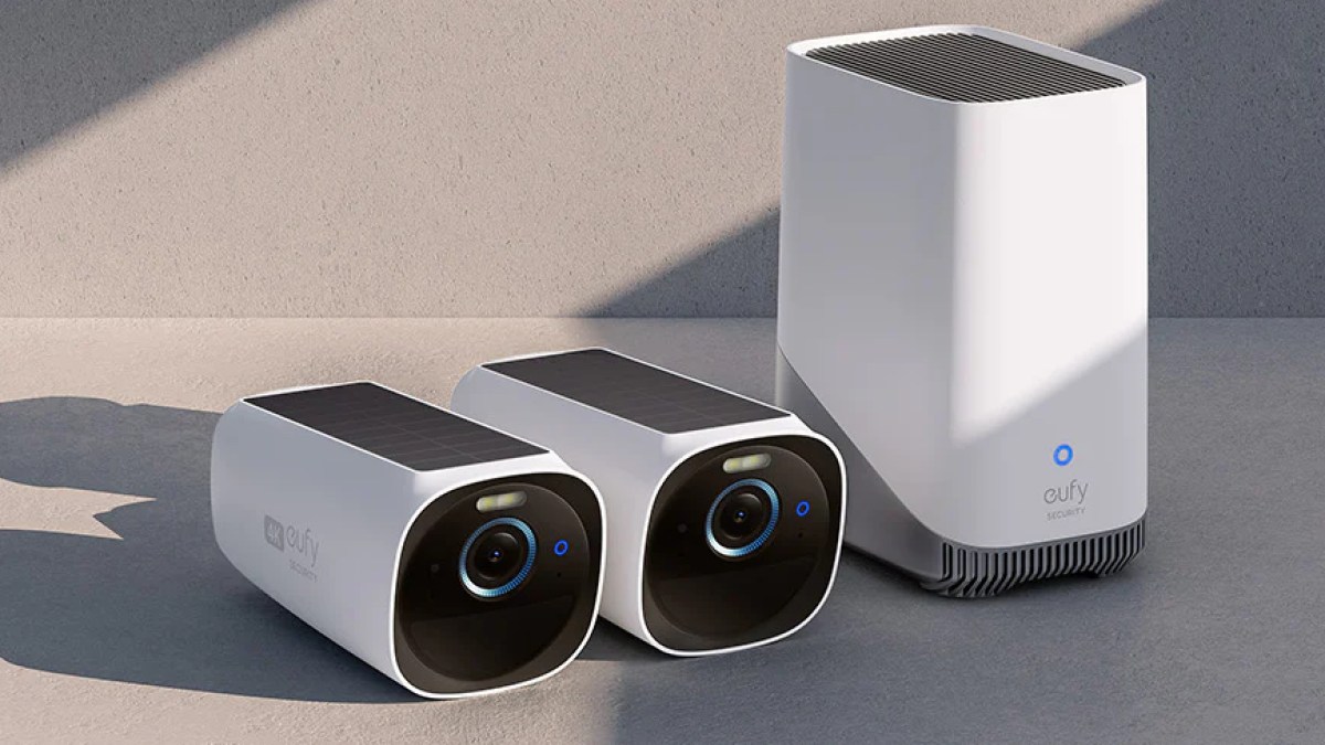 Two Eufy S330 cameras lay next to a HomeBase hub on a gray surface, light by bright lights.