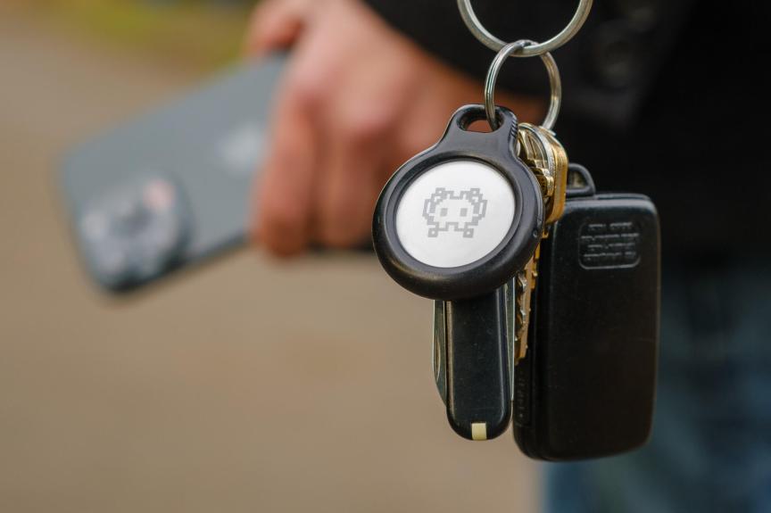 An AirTag on a keychain worn by a person carrying iPhone.