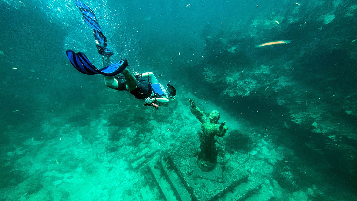 A diver swims near a submerged statue of Christ in the ocean