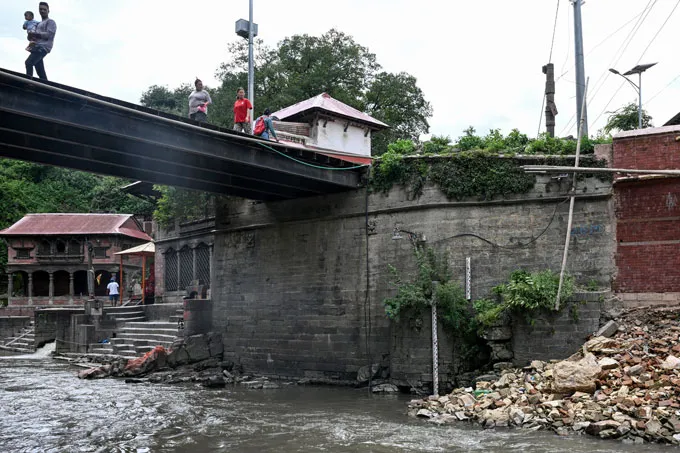 Several people walk over a bridge in Kathmandu that has a siren designed to provide flood warnings.