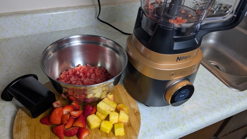 Ninja-CrushBoss-food-processor-next-to-bowl-of-diced-watermelon-and-fresh-fruit-on-cutting-board